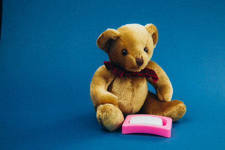 Toy bear sits with toy soap on a blue background.の写真素材