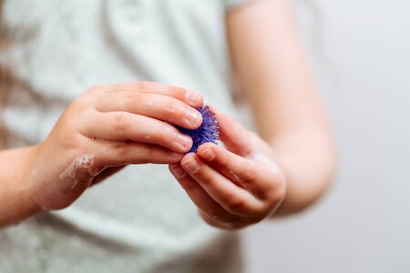 Girl with hands in soap holds an abstract model of coronavirus. Protect yourself, wash your hands.の写真素材