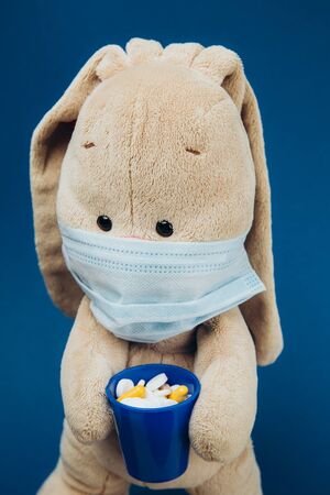 The toy bunny wears a protective medical mask. Flapper holds a glass of pills. Stop coronavirus. Medicine conceptの写真素材