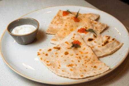 Yantyk with salmon, red caviar, served with sour cream sauce. Lies on a white, round plate.
