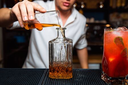 The barman pours whiskey into a transparent decanter.の写真素材