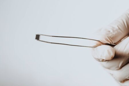 A hand in a white glove holds a chip with tweezers. Chipization of people after an epidemic coronavirus.の写真素材