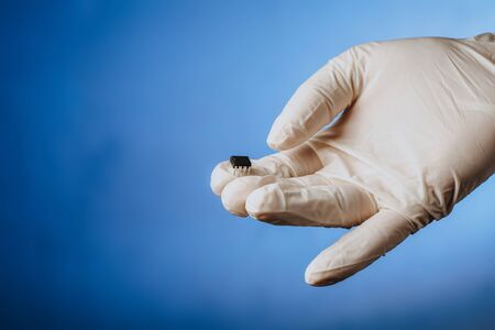 Hand in a white glove holds a chip. Chipization of people after an epidemic coronavirus. Copy spaceの写真素材