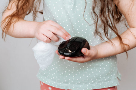 A girl wipes a computer mouse with a disinfectant wipe. Concept of disinfecting surfaces from...