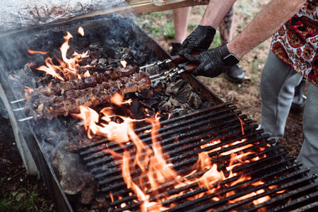 The cook prepares meat-kebab, cut into pieces, barbecue. The meat is strung on three skewers.