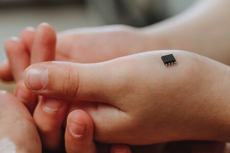 A small black chip lies on the palm of the hand of a child. Chipization of people after an epidemic coronavirus. の写真素材