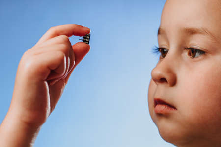 A girl holds in her hand and examines a small black chip.の写真素材