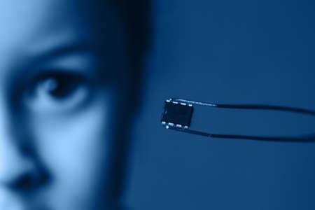 A tweezers holds a black microchip on the background of the face.の写真素材