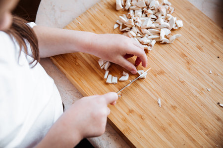 Fresh champignon mushrooms on a wooden board. Girl cuts mushrooms with a knife.