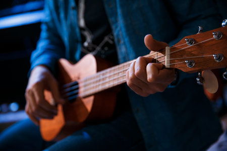 A young man plays the guitar while sitting.