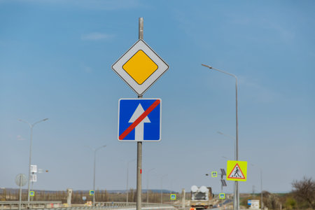 Road sign main road and one-way road end sign on the background of the road and blue sky.