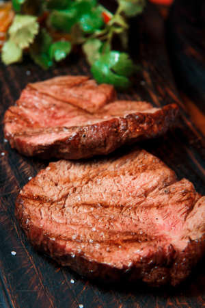 Thick juicy portions of fried fillet steak are served, sprinkled with salt, on an old wooden board. The dish is ready to serve.の写真素材