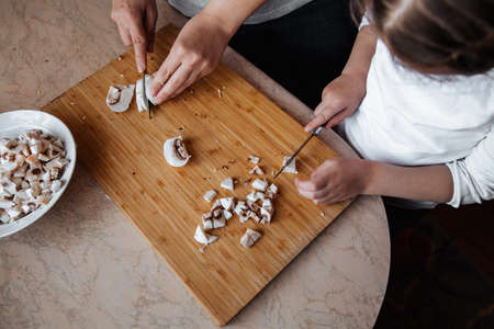 Fresh champignon mushrooms on a wooden board. A girl and her mother cut mushrooms with a knife. Time spent together. Family conceptの写真素材