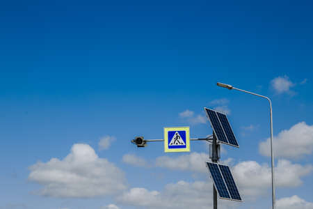 The pedestrian crossing sign powered by solar panels installed above. Traffic signs and rules. Against the background of a blue sky with cloudsの写真素材