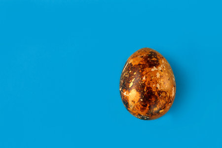 Easter egg painted orange with gold. One painted easter egg on a blue background.Flat lay. Copy space.の写真素材