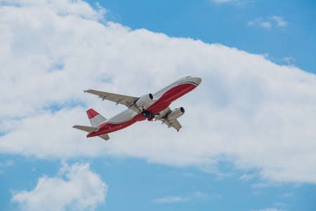 Passenger plane of white-red color flies in the blue sky with white clouds, air transportation concept, population evacuationの写真素材