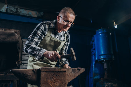 Senior an artisan blacksmith knocks with a hammer on iron to shape