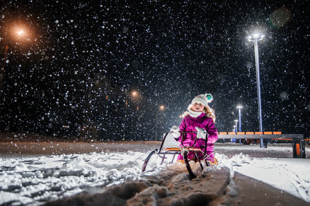 A little girl is sledding in the evening.