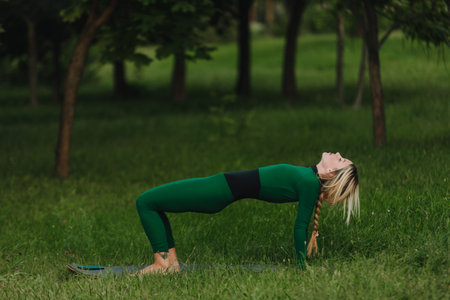 A woman is learning yoga on a yoga mat in the park on a body summer evening