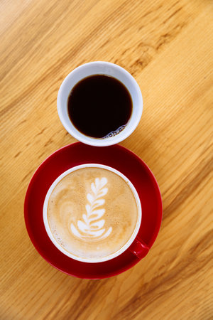 Coffee in a red cup with milk and latte art and coffee in a white cup on a tableの写真素材