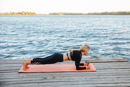 A young woman is doing a plank on a yoga mat by the river.の写真素材