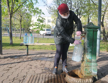 A woman in a medical mask draws water from a pump room column during quarantine in Kiev, April 20, 2020.のeditorial素材