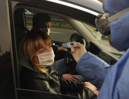 A medical professional conducts a temperature examination at a checkpoint at the entrance to Kiev, April 16, 2020.のeditorial素材