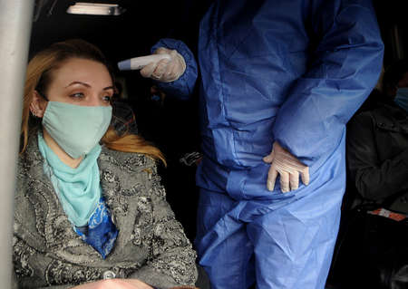 A medical professional conducts a temperature examination at a checkpoint at the entrance to Kiev, April 16, 2020.のeditorial素材