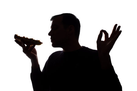 Portrait of a young man satisfied with the taste of pizza, unshaven, side view - dark isolated...