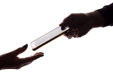 The hand of a young man gives a smart phone to an elderly woman - silhouette, help conceptの写真素材