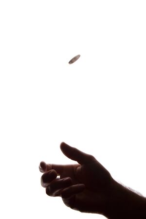 Young man hand with a coin between his fingers - silhouette, concept of moneyの写真素材