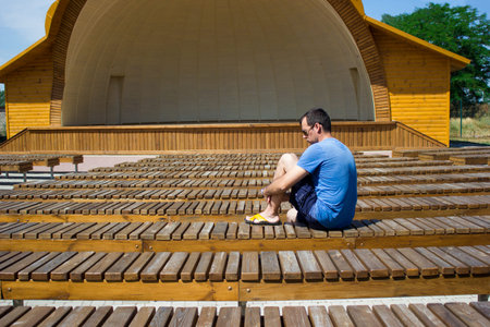 The man is sitting alone in her back among the many benches of the street theater