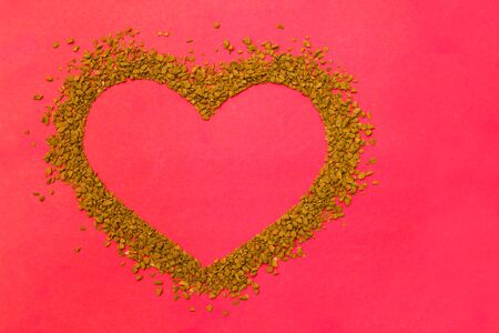 Dry instant coffee granules in the shape of a heart - brown texture, on a red backgroundの写真素材