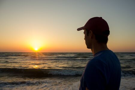 Portrait of a young man in cap on the beach - at sunriseの写真素材