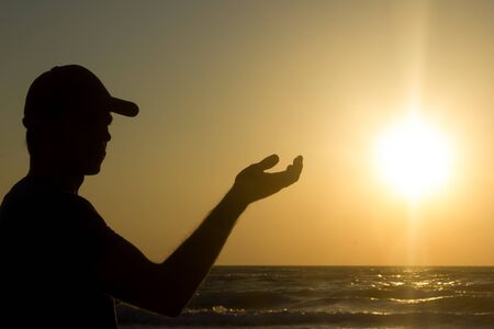 Portrait of a young man in cap on the beach - reached out to the sunの写真素材