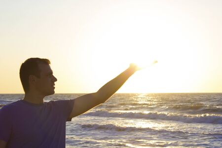 Young man clicks sunrise on a background of blue sky and sea, horizon beach dawnの写真素材