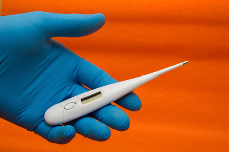 Hand in a medical glove holds an electronic thermometer - temperature measurement, coronavirus,...