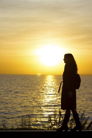 Girl walks on railroad tracks in a coat and boots on a sunset background - travel, depression, lifestyleの写真素材