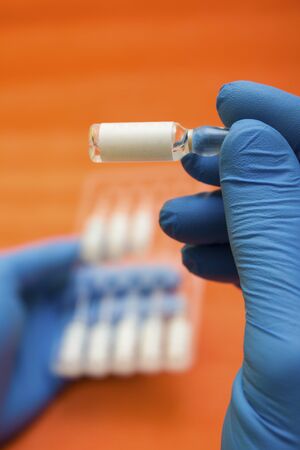 Ampoules with a medicine for a vaccine against diseases, flu in the hands of a medic with gloves - search for a vaccine, treatment of influenza, coronavirus, covid19の写真素材