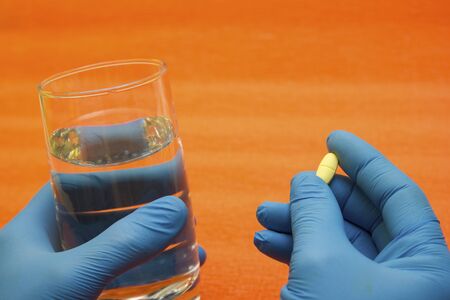 Hands in medical gloves take a pill with a glass of water - choice of medicine, doctors are sick, coronavirus, covid19の写真素材