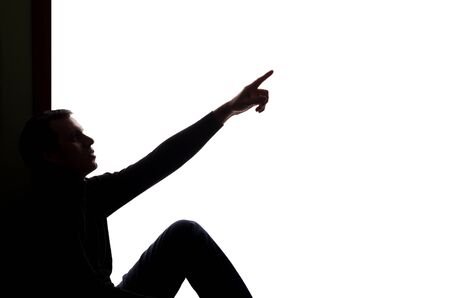 Young man sitting shows his index finger forward - silhouetteの写真素材