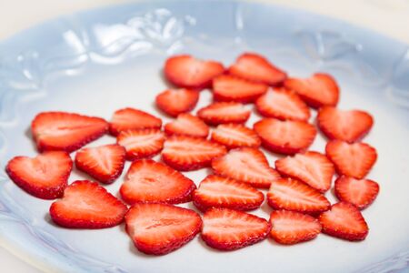 Beautiful heart symbol from chopped red juicy strawberry - on a blue plateの写真素材