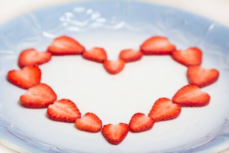 Beautiful heart symbol from chopped red juicy strawberry - on a blue plateの写真素材