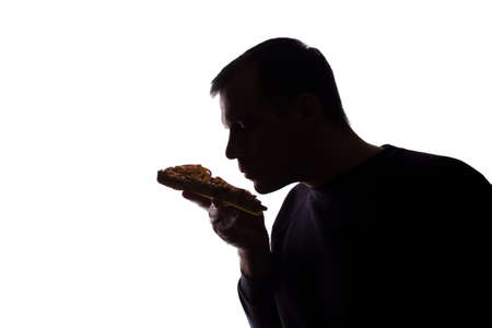 Portrait of a young man satisfied with the taste of pizza, unshaven, side view - dark isolated silhouetteの写真素材