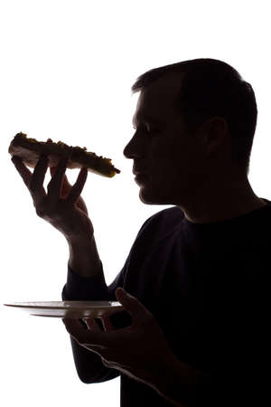Portrait of a young man eat a pizza in hand, unshaven, side view - dark isolated silhouetteの写真素材