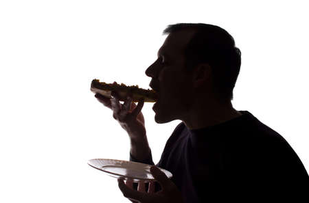 Portrait of a young man eat a pizza in hand, unshaven, side view - dark isolated silhouetteの写真素材