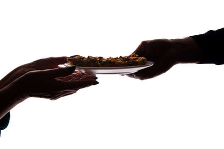 Young man gives a pizza on dish to an elderly woman in her hand - silhouette, help conceptの写真素材