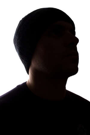 Portrait of a young man, unshaven, side view in cap - dark isolated silhouetteの写真素材
