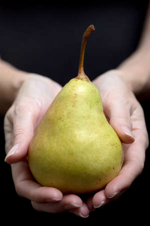 Yellow pear on a woman's hand on black background - horizontalの写真素材