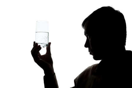 Young man drinking a glass of sparkling water, checks the quality - silhouetteの写真素材